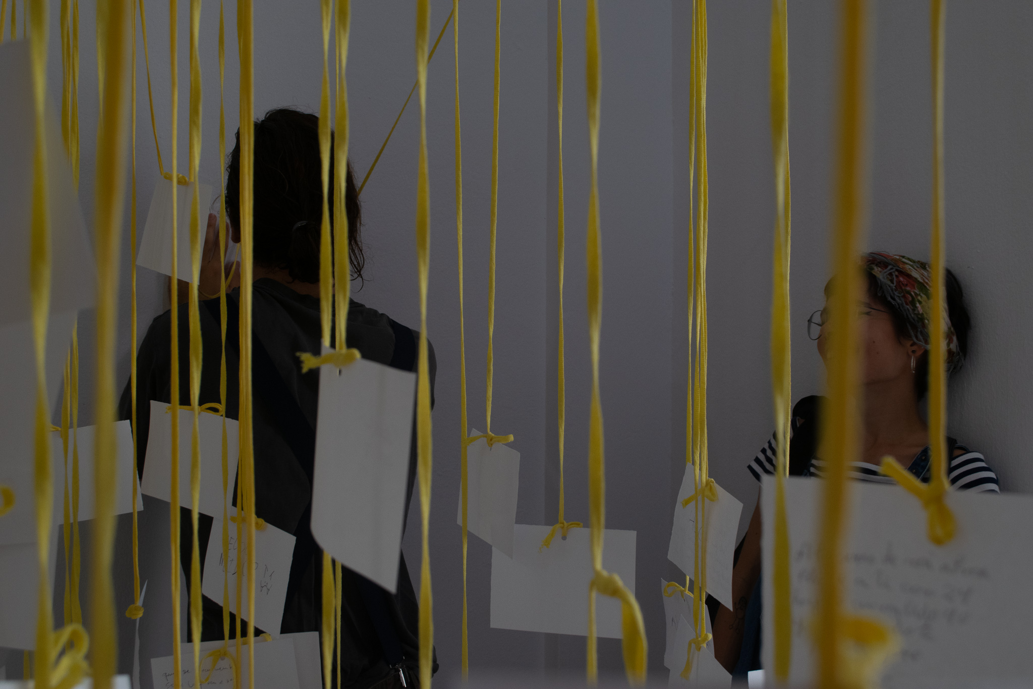Fotografía de dos personas al fondo y en primer plano unas cuerdas colgando notas de papel.