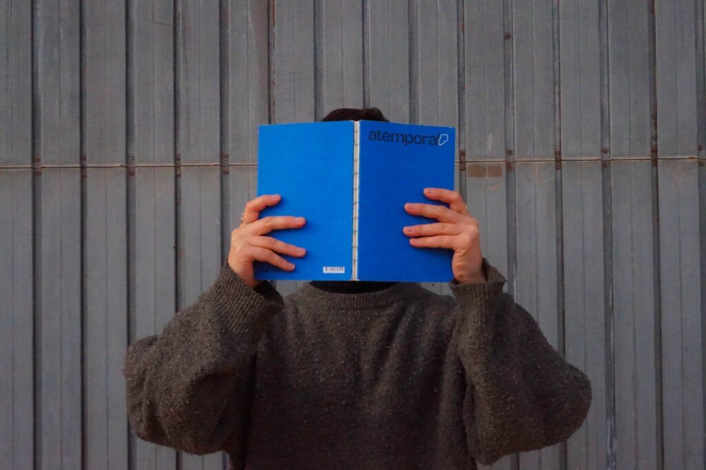 escritura por encargo: una persona con un jersey gris se tapa el rostro con un libro azul